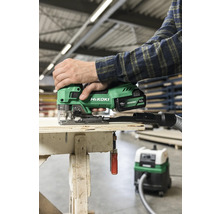 Une personne utilise une scie sauteuse sans fil verte Hikoki sur une surface en bois avec un aspirateur branché.
