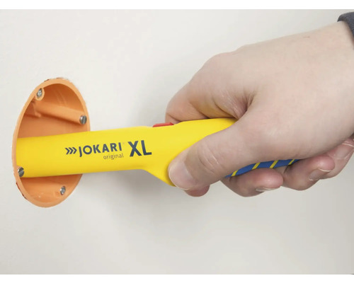 Main tenant un dénudeur de câbles Jokari XL sur une boîte de dérivation murale