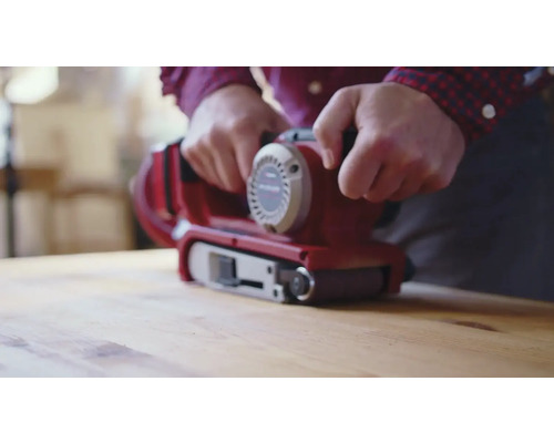 Eine Person benutzt einen Bandschleifer auf einer Holzoberfläche.