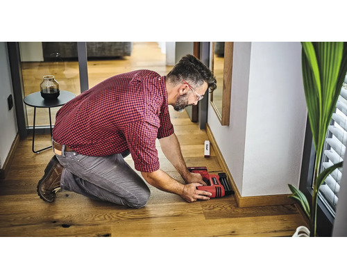 Mann befestigt Sockelleisten mit einem Elektrotacker an einer Wand