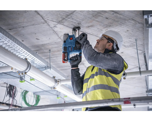 Un homme fixe un support à un plafond en béton à l'aide d'un perforateur sans fil.