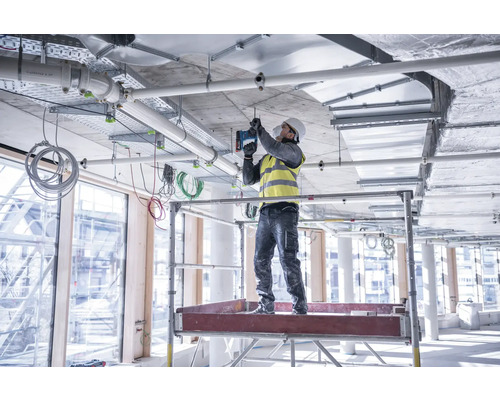 Un ouvrier du bâtiment se tient sur un échafaudage et fixe une installation au plafond.