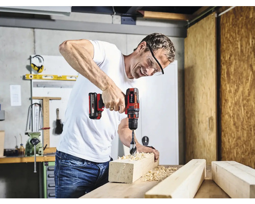 Ein Mann bohrt mit einem Akku-Bohrschrauber in ein Holzstück in einer Werkstatt.