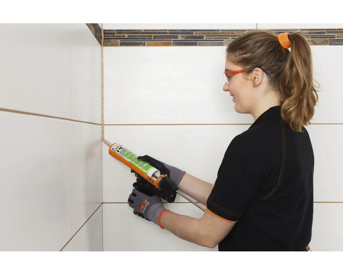 Frau dichtet Fugen zwischen Fliesen mit Silikon ab.