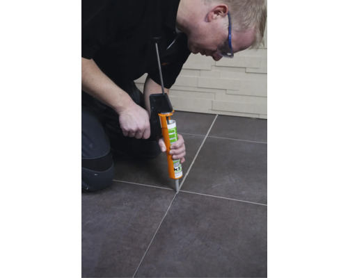 Handwerker, der mit einer Fugenpistole Fugenmasse zwischen Fliesen aufträgt.