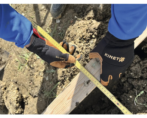 Une personne mesure une planche de bois avec un mètre ruban, tout en portant des gants de travail.