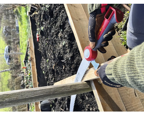 Une personne scie une planche de bois avec une scie à main dans le jardin.