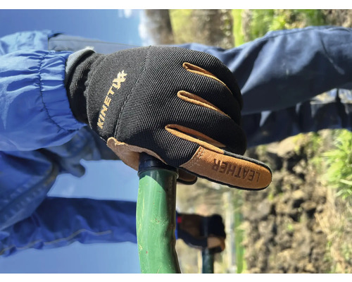 Main avec des gants de travail Kinetix sur un outil de jardin