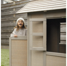 Un enfant joue dans une cabane en bois dans le jardin.
