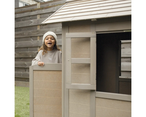 Un enfant joue dans une cabane en bois dans le jardin.