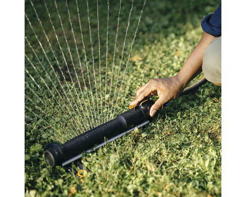 Eine Person bedient einen Rasensprenger auf einem Rasen.