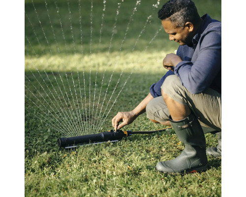 Eine Person stellt einen Rasensprenger im Garten ein.