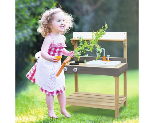 Mädchen spielt mit einer hölzernen Outdoor Spielküche mit Spüle und Herdplatten im Garten.