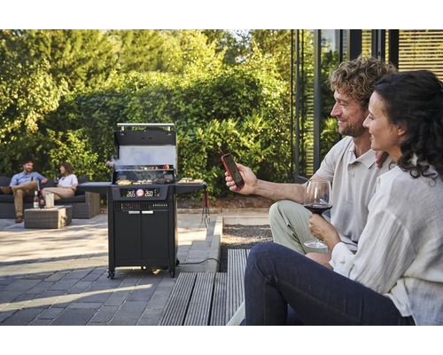 Scène avec un gril à charbon de bois, deux personnes au premier plan et deux personnes sur un canapé à l''arrière-plan.