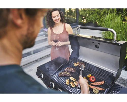 Personen grillen Steaks und Gemüse auf einem Grill im Freien.