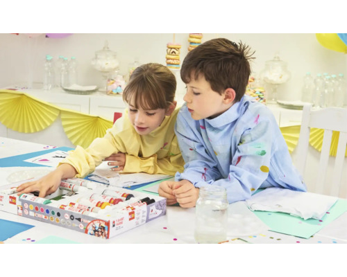 Zwei Kinder bemalen T-Shirts mit Textilfarbe an einem Tisch.