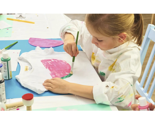 Ein Kind bemalt ein T-Shirt mit einem Pinsel.