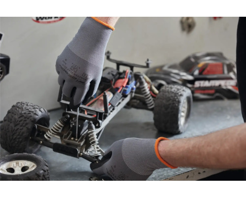 Un homme répare une voiture miniature avec des gants de protection.