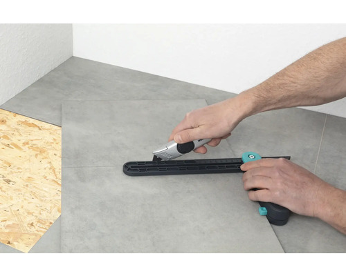 Person schneidet Fliesen mit einem Fliesenschneider und einem Cuttermesser