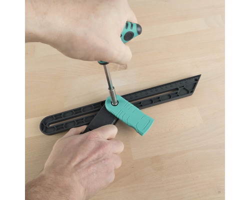 Eine Person justiert eine Winkelspinne mit einem Schraubendreher auf einem Holzboden.