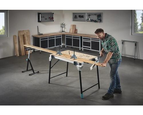 Werkstatteinrichtung mit Werktisch, Holzplatten und Heimwerker beim Sägen eines Brettes