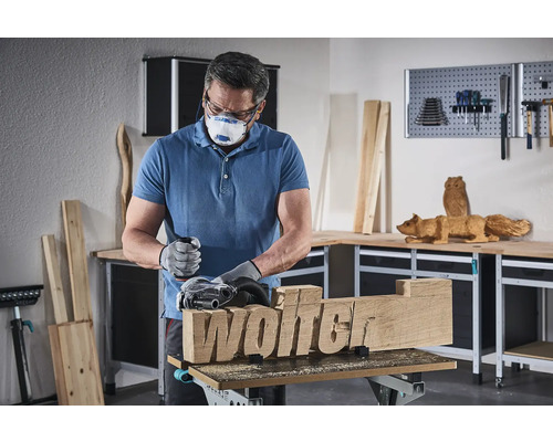 Un homme ponce un morceau de bois avec l''inscription Wolter à l''aide d''une ponceuse.