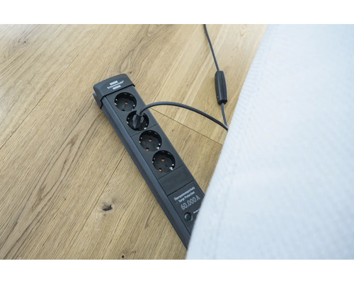 Steckdosenleiste mit Überspannungsschutz und angeschlossenem Stecker auf einem Holzboden