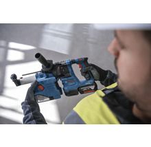 Un ouvrier tient un marteau perforateur bleu Bosch avec une batterie 18 volts.