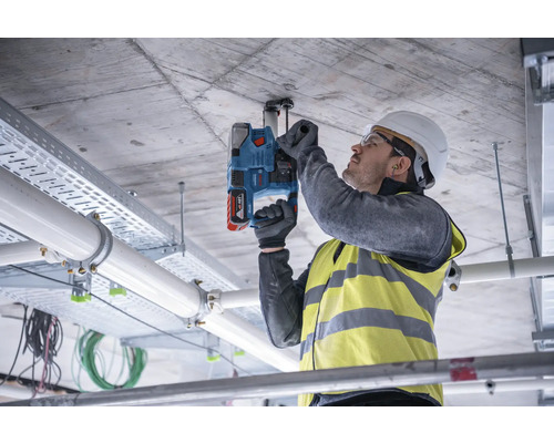 Un homme perce un plafond en béton avec une perceuse à percussion pour fixer une fixation.