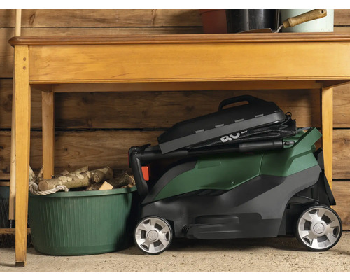 Tondeuse à gazon pliée sous une table en bois dans un garage.