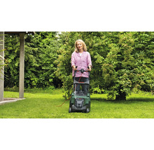 Frau benutzt einen Rasenmäher im Garten.