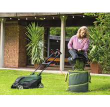 Frau leert Gras aus einem Rasenmäher in einen Gartensack im Garten.