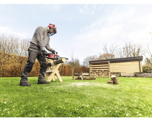 Une personne coupe du bois avec une tronçonneuse sur une structure en bois dans le jardin.