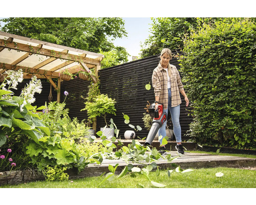 Frau benutzt einen Akku-Laubbläser zur Gartenarbeit in einem gepflegten Garten