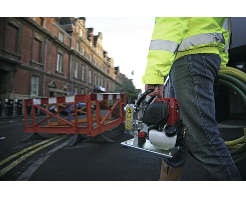 Un ouvrier du bâtiment transporte une pompe à eau mobile sur un chantier.