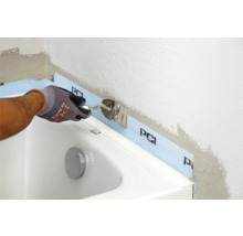 Ein Handwerker verwendet einen Spachtel zum Auftragen von Dichtmasse im Badezimmer entlang einer Badewanne mit PCI Dichtband.
