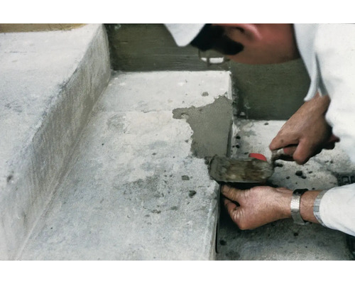 Eine Person repariert eine Betontreppe mit Mörtel und einer Kelle.