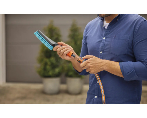 Un homme raccorde une brosse à un tuyau d''arrosage pour des travaux de nettoyage à l''extérieur.