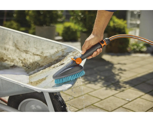 Une personne nettoie une brouette avec une brosse et un tuyau d''arrosage