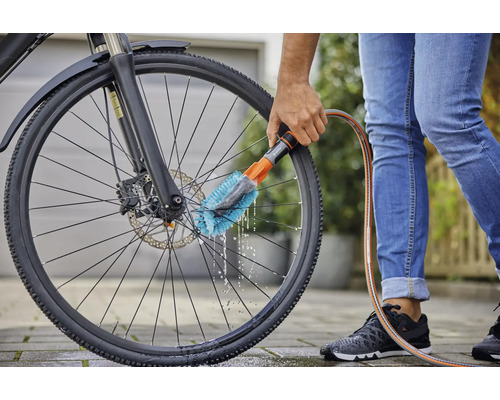 Une personne nettoie une roue de vélo avec une brosse et un tuyau d''arrosage