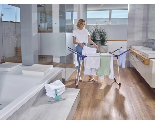 Frau hängt Wäsche auf einem Wäscheständer in einem hellen Badezimmer.