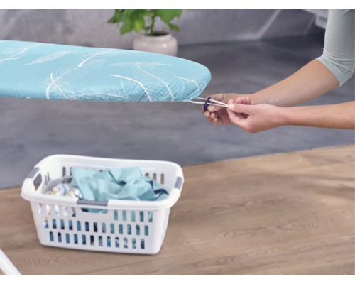 Person befestigt einen Bügelbrettbezug mit Gummizug, Wäschekorb im Vordergrund