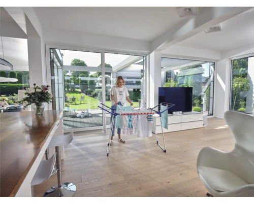 Frau hängt Wäsche auf einem Wäscheständer in einem hellen Wohnzimmer.