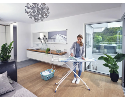 Frau bügelt Wäsche auf einem Bügelbrett in einem hellen Raum.