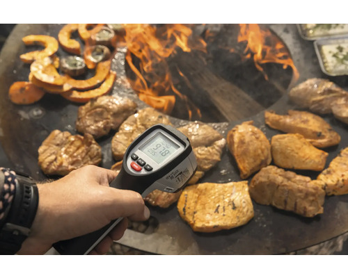 Une personne mesure la température des aliments avec un thermomètre infrarouge au-dessus d''un feu ouvert.