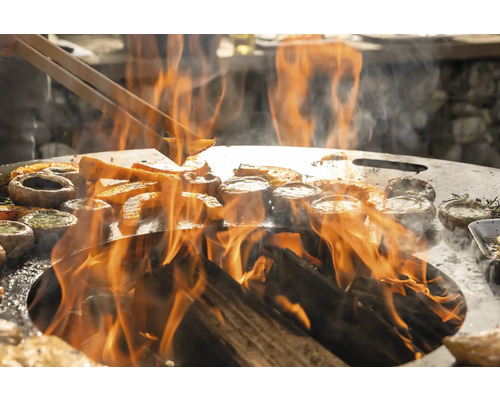 Des légumes et des champignons sont préparés sur une plaque de cuisson au-dessus d''un feu ouvert.