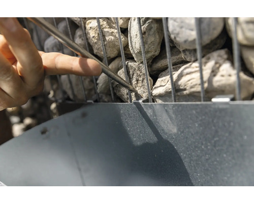 Nahaufnahme einer Gabione, die mit Steinen gefüllt und mit einem Werkzeug bearbeitet wird.