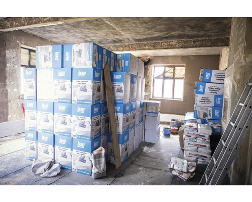 Baustelle mit gestapelten Knauf Dämmplatten und Säcken mit Baumaterial.