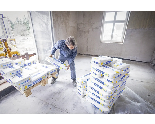 Un homme décharge des sacs d''enduit intérieur dans une pièce. Des palettes d''enduit intérieur sont livrées.