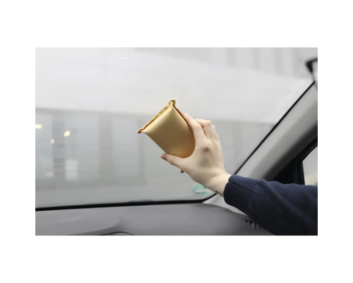 Une personne nettoie un pare-brise de voiture avec un tampon de nettoyage.